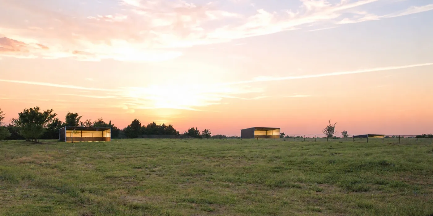 Open pasture at sunset, with run-in shelters along the fence line.