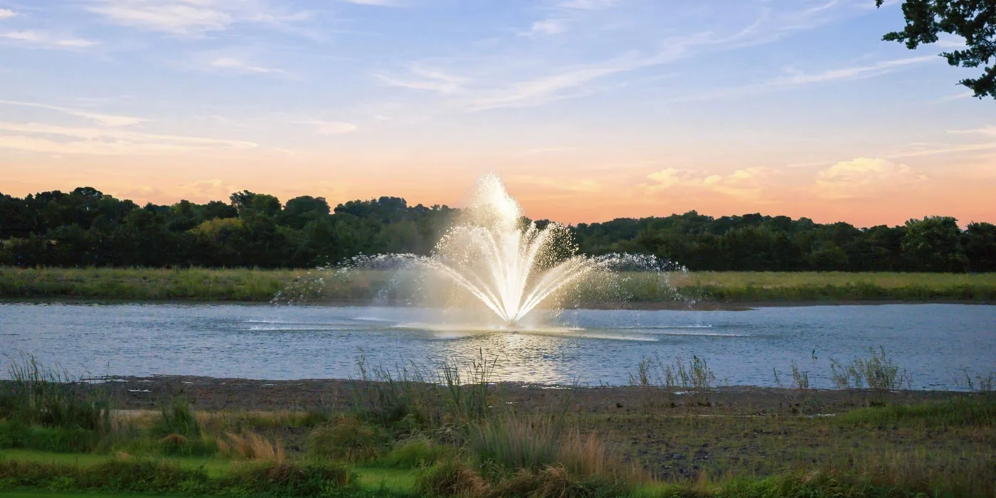 A fountain playing on the pond at sunset.