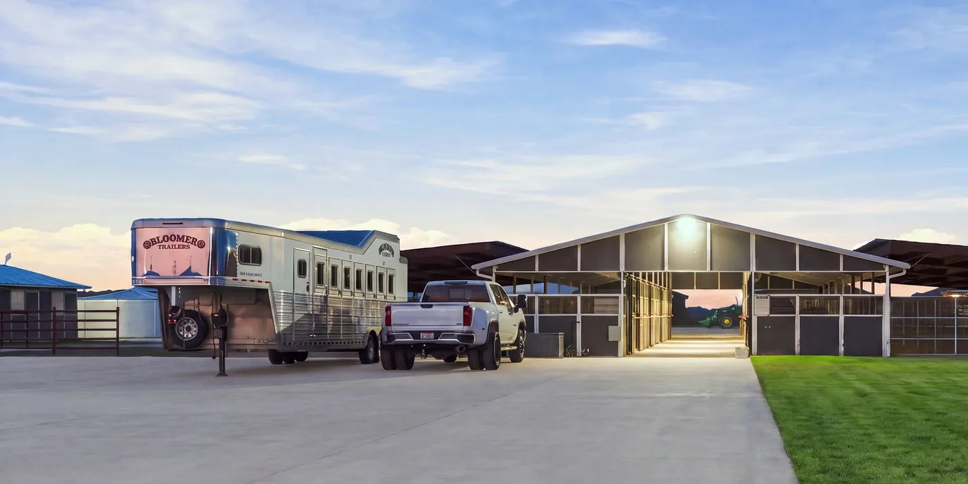A truck and horse trailer parked beside the covered barn at dusk.